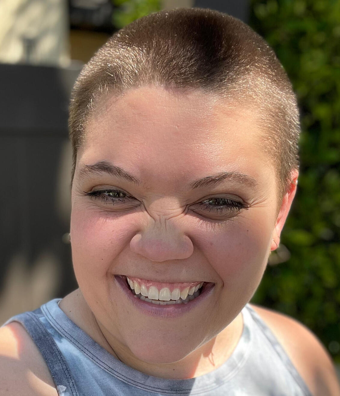 This is a picture of Evan smiling. Their nosed is scrunched up in a way that's pretty cute. They have a buzzcut too.